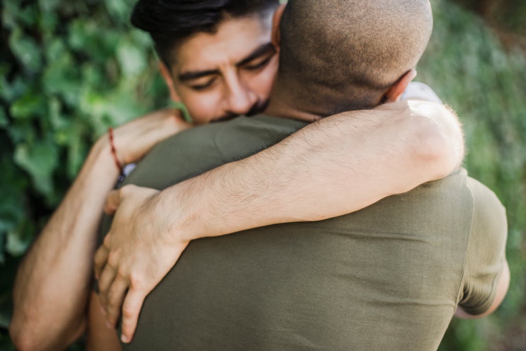 Intimate moment between two men sharing a warm hug outdoors, captured in natural light.